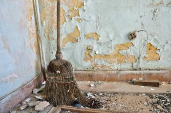 Dusty straw broom on filthy floor of abandoned house.