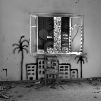 Chair under broken window in abandoned interior. City graffiti painted on the wall.