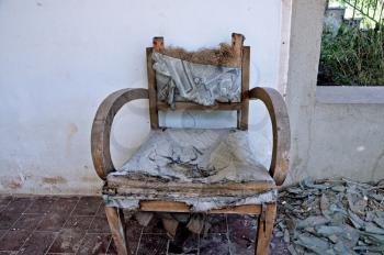 Torn armchair and pile of broken glass on the porch of an abandoned house.
