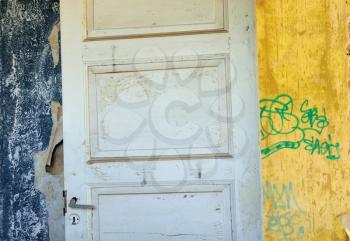 Wooden door, torn vintage wallpaper and peeling walls in abandoned interior.