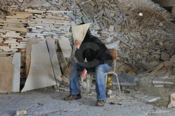 Man under pile of broken marble scrap pieces. Obscured figure in industrial interior.
