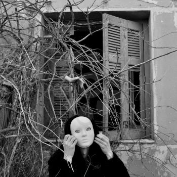 Figure with white mask under window with overgrown plants and doll hand. Black and white.