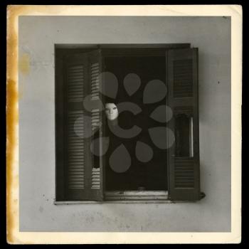 Vintage photograph of masked figure by the broken windows of abandoned house.