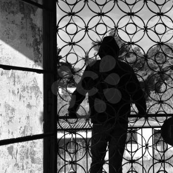 Man on the balcony of an abandoned house, metal door pattern. Black and white.