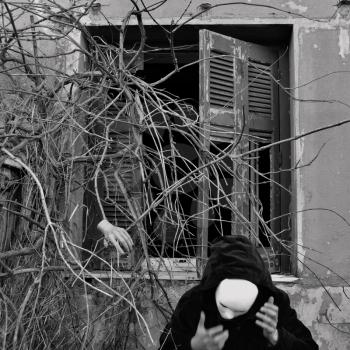 Masked figure in black and overgrown dead plants. Black and white, motion blur.