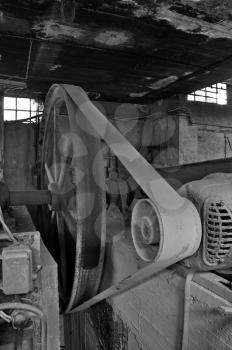Rusty wheel belt driven machinery in abandoned factory interior. Black and white.