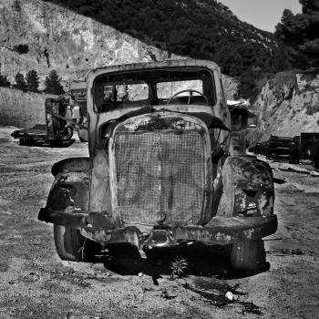 Rusty abandoned car and industrial machinery at a quarry. Black and white.