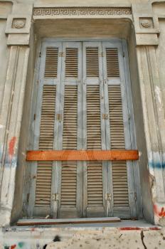 Boarded up window with decorative meander pattern and weathered wall of a neoclassical building in Athens, Greece.