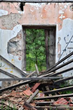 Collapsed roof chipped wall and open door with view to nature scene. Abandoned house interior.