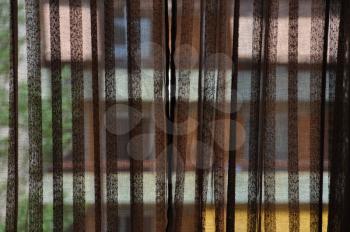 Brown transparent curtains and distorted colorful building in the background.