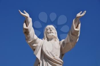 Jesus Christ with hands raised in blessing under blue sky. Marble funerary statue.