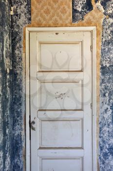 Shut wooden door peeling wall and torn vintage wallpaper in abandoned house.