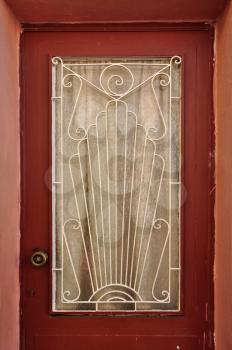 Old wooden door glass lite screen decorated with iron pattern of abstract sun rays and spiral symbols.