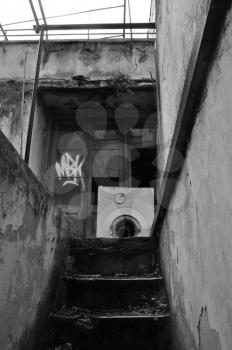 Basement stairs and abandoned house exterior with broken washing machine on rainy day. Black and white.
