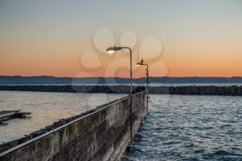 A heron sits on a lamp post at the marina in Des Moines, Washington at sunset.
