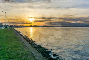 The sun is sinking toward the horizon at Alki Beach in West Seattle, Washington.