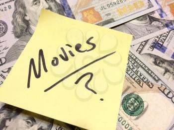 American cash money and yellow post it note with text Movies with question mark in black color aerial view