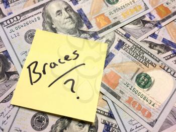 American cash money and yellow post it note with text Braces with question mark in black color aerial view