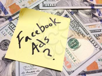 American cash money and yellow paper note with text Facebook Ads with question mark in black color aerial view