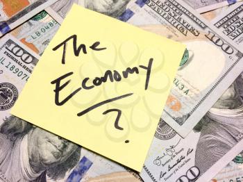 American cash money and yellow paper note with text The Economy with question mark in black color aerial view