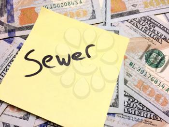 American cash money and yellow sticky note with text Sewer in black color aerial view
