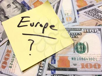 American cash money and yellow sticky note with text Europe with question mark in black color aerial view