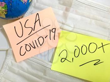 USA Coronavirus COVID-19 infection medical cases and deaths United States. China COVID respiratory disease influenza virus statistics hand written on surgical mask and earth globe background