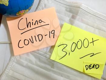 Coronavirus COVID-19 China infection medical cases and deaths. COVID respiratory disease influenza virus statistics hand written on surgical mask and earth globe background
