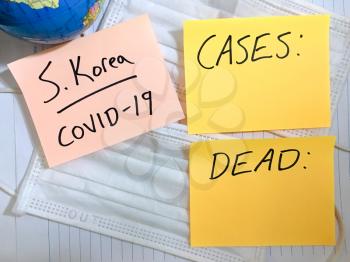 Coronavirus COVID-19 South Korea infection medical cases and deaths. China COVID respiratory disease influenza virus statistics hand written on surgical mask and earth globe background