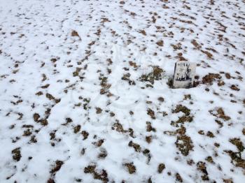 Solitary headstone at graveyard cemetery with snow on white winter day