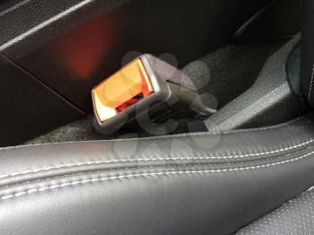 Seat belt lock in car made of black plastic near leather stitched seat