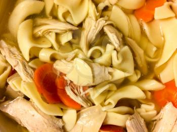 Chicken noodle soup overhaed view with carrot on homestyle floral table cloth
