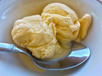 Vanilla ice cream in bowl with spoon melting golden yellow color