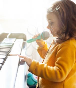 Girl toddler plays the piano and sings with the toy microphone.