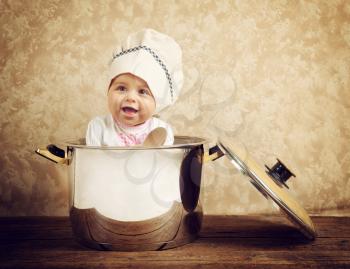 Cute baby chef in a huge cauldron on wooden table
