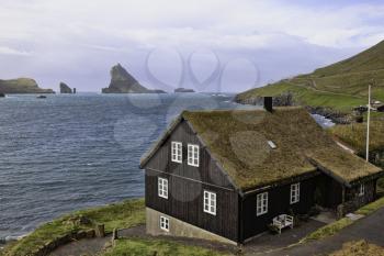 Bour, Faroe Islands - 14 September 2019 - Typical faroe house with grassy roof and Tindholmur and Drangarnir on the background