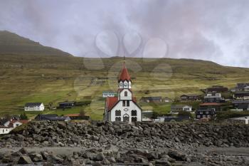 Sandavagur Church with red roof also called Sandavags Kirkja and the river Stora located in the picturesque village of Sandavagur on Faroe Islands, Denmark