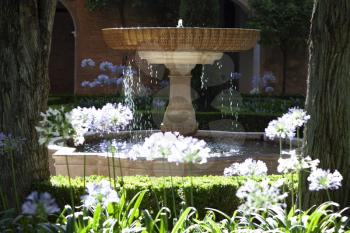 Fountain in Alhambra lit by the sun and surrounded by flowers