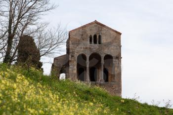 Oviedo, Spain - 11 December 2018: Church of St Mary at Mount Naranco with the field of yellow flowers