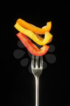 Three different kind of pepper, red, orange and yellow on a fork on a black background