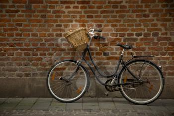 Black bicycle with straw basket along a brick wall
