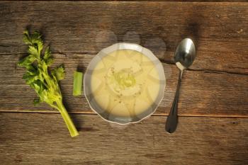 Top view of a bowl of celery soup, spoon and branch of celery on a rustic background