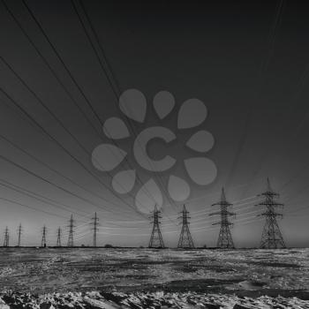 Group of high-voltage electricity power pylons in black and white and snow covered countryside, Canada