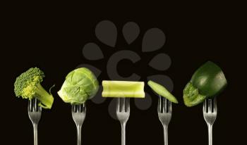 Variation of green vegetables on a black background, broccoli, brussels sprout, celery, green bean and zucchini.