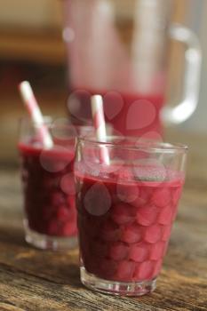 Raspberry smoothies with a pink lined straw and a pitcher on a rustic background