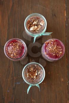 Top view of healthy chocolate chia pudding with berry coulis on top with nuts and spoon on a wooden background