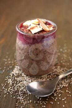 Healthy chocolate chia pudding surround by chia seeds with berry coulis on top and coconut on a wooden background