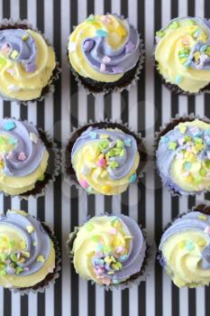 Top view of nine yellow and lilac cupcake on a black and white lined background