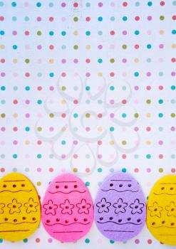 Decorated felt easter eggs yellow, pink, and lilac on a polka dots background