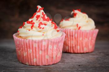 Two cupcakes with vanilla icing and red candies in a pink polka dots paper.